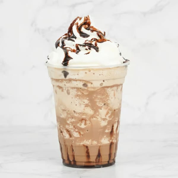 A chocolate mocha frappe with whipped cream and chocolate drizzle in a clear plastic cup.